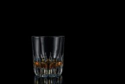 Cut glass tumbler a third filled with whiskey on a black background